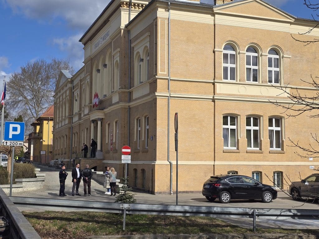 Budynek urzędu miejskiego w Ostr&oacute;dzie, na zewnątrz stoją policjanci i pracownicy, trwa ewakuacja po alarmie.