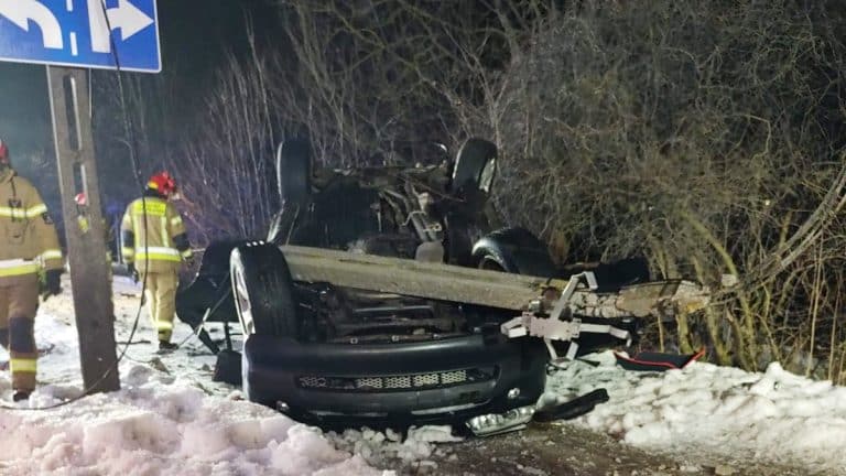 Rozbity samoch&oacute;d BMW na dachu na śniegu, służby ratunkowe na miejscu zdarzenia.