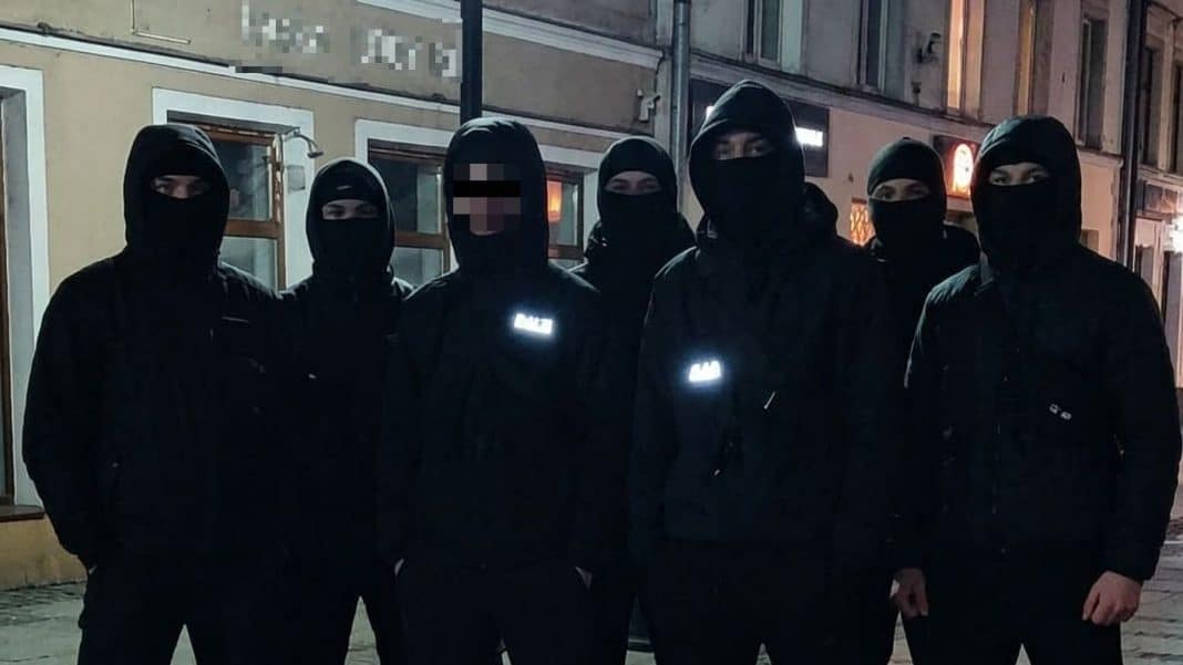 Grupa policjant&oacute;w w maskach na tle miasta nocą, w ciemnych ubraniach, w centrum Olsztyna.