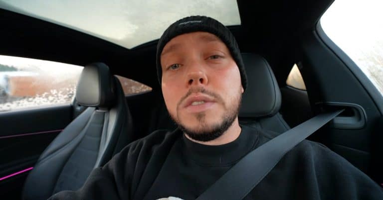 Mężczyzna w czapce siedzi w samochodzie, w tle widoczna deszczowa pogoda za oknem.