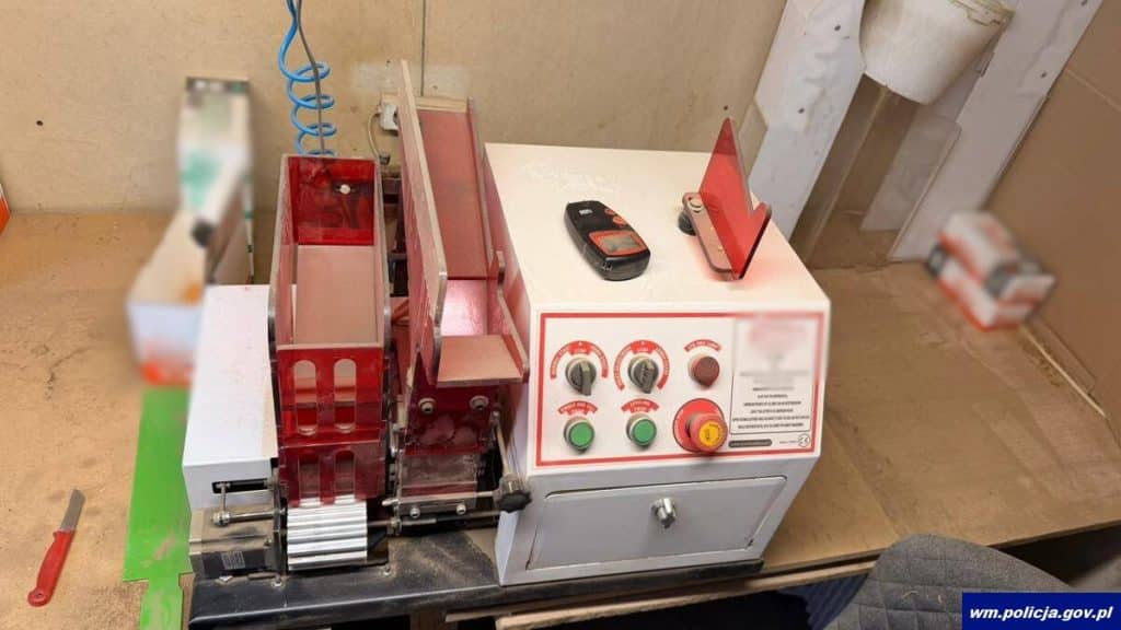 Urządzenie do produkcji papieros&oacute;w na stole, obok telefon i narzędzia, w pomieszczeniu.