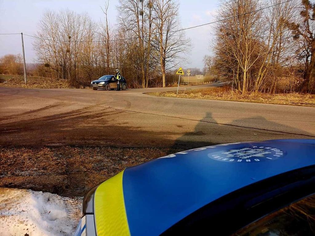Policjant przeprowadza kontrolę na bocznej drodze, widoczny radiow&oacute;z i znaki ostrzegawcze.