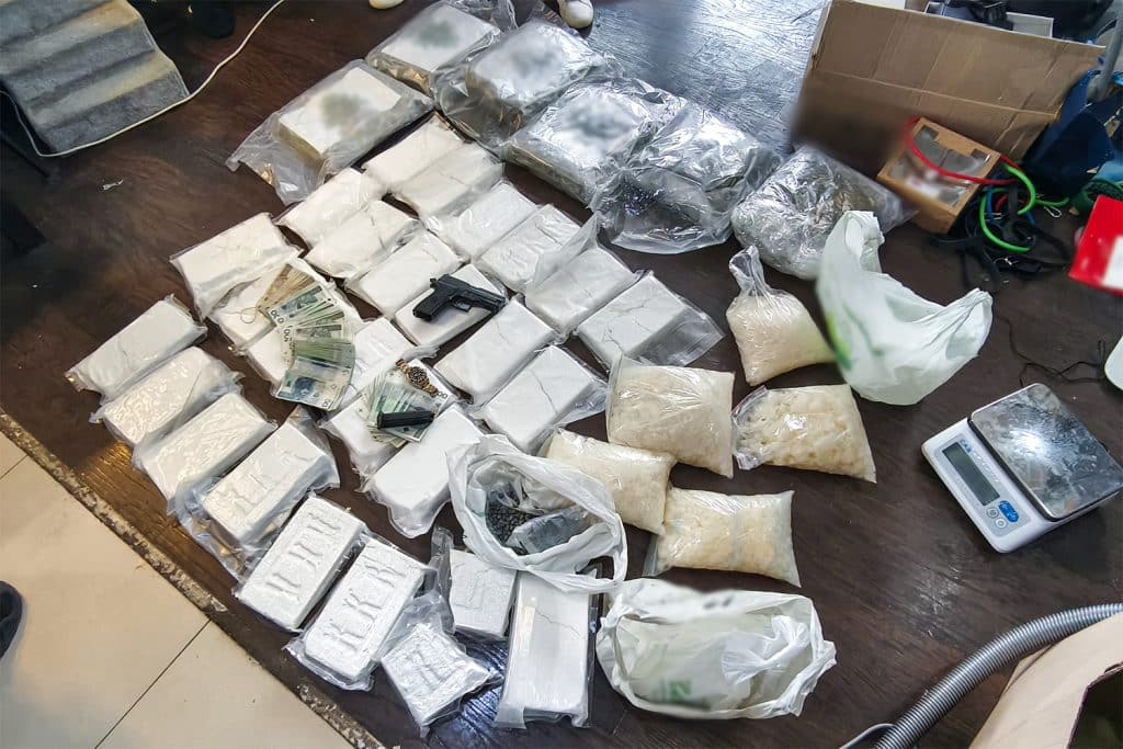 Na zdjęciu widoczne są pakiety z nielegalnym towarem, broń i pieniądze na stole podczas akcji służb.