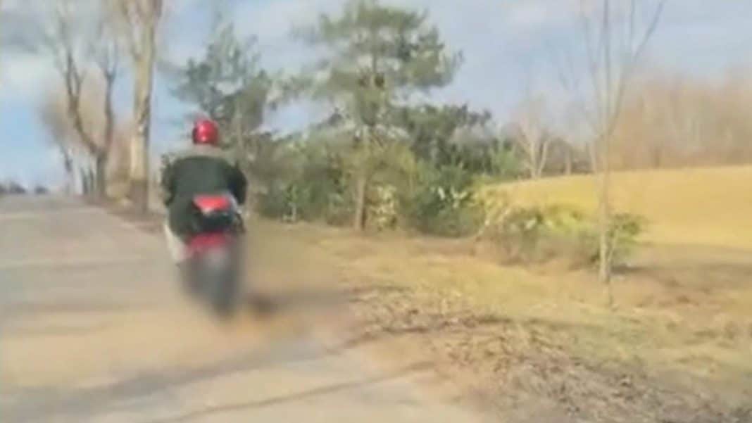 Mężczyzna ciągnący psa na sznurku za motorowerem na mazurskiej drodze.