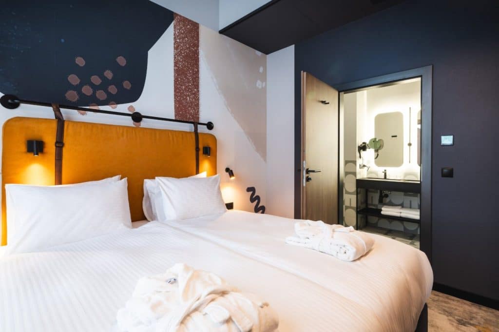 Wnętrze nowoczesnego hotelowego pokoju z dużym ł&oacute;żkiem i łazienką w tle.