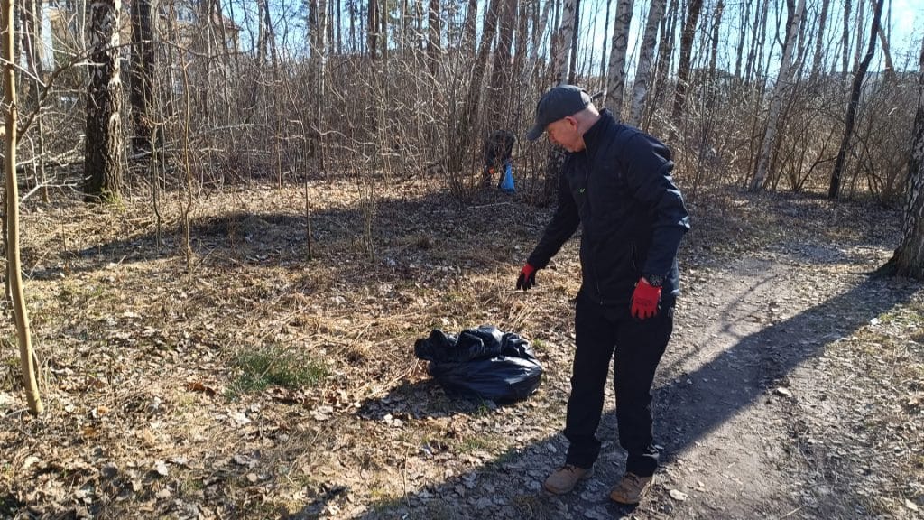 Mężczyzna sprzątający las w słoneczny dzień, zbierający odpady w czarną torbę.