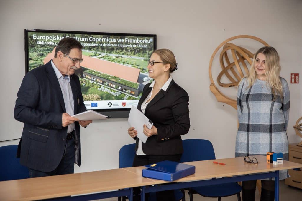 Trzy osoby rozmawiają przy stole podczas prezentacji projektu Centrum Copernicus, w tle ekran z wizualizacją inwestycji.