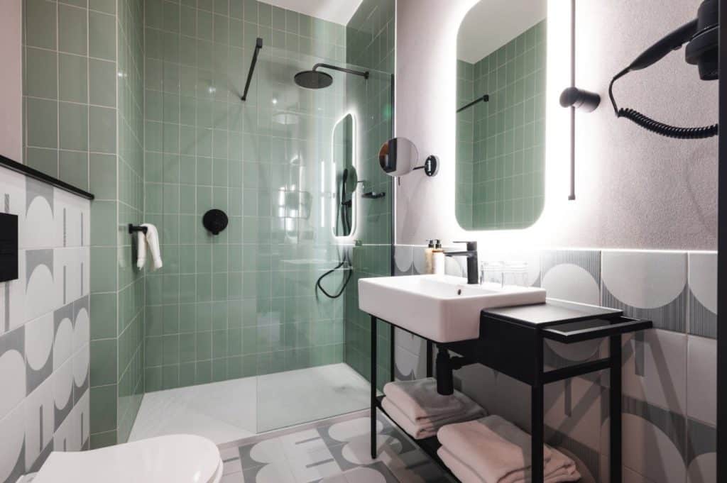 Nowoczesna łazienka w hotelu z zielonymi płytkami i minimalistycznym wyposażeniem.