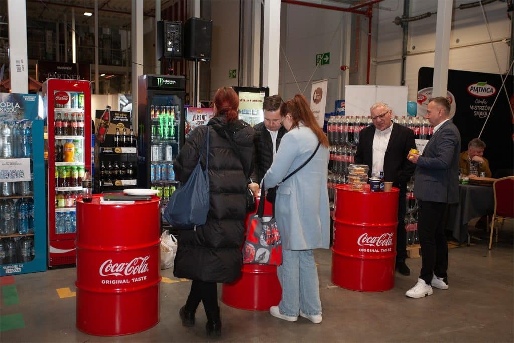 Uczestnicy targ&oacute;w biznesowych w Gdańsku rozmawiają przy stoiskach z napojami i produktami.