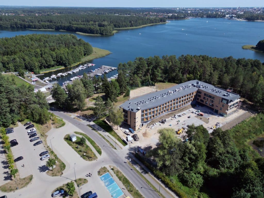 Widok na jezioro Ukiel z otwartym portem jachtowym i otaczającą zieleń, w tle zabudowa miasta.