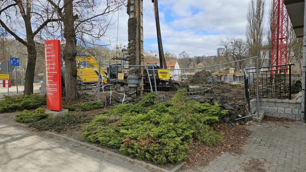 Trwa budowa nowego obiektu usługowego w centrum Olsztyna, widoczne wykopy i prace ziemne na placu budowy.
