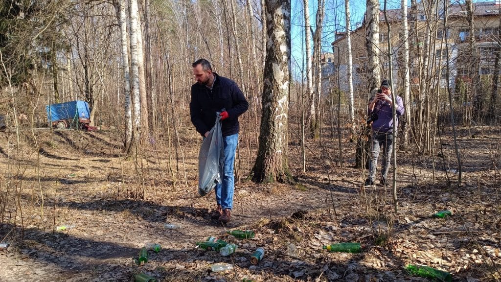 Grupa mieszkańc&oacute;w i prezydent sprzątają las w Olsztynie, zbierając odpady w słoneczny dzień.