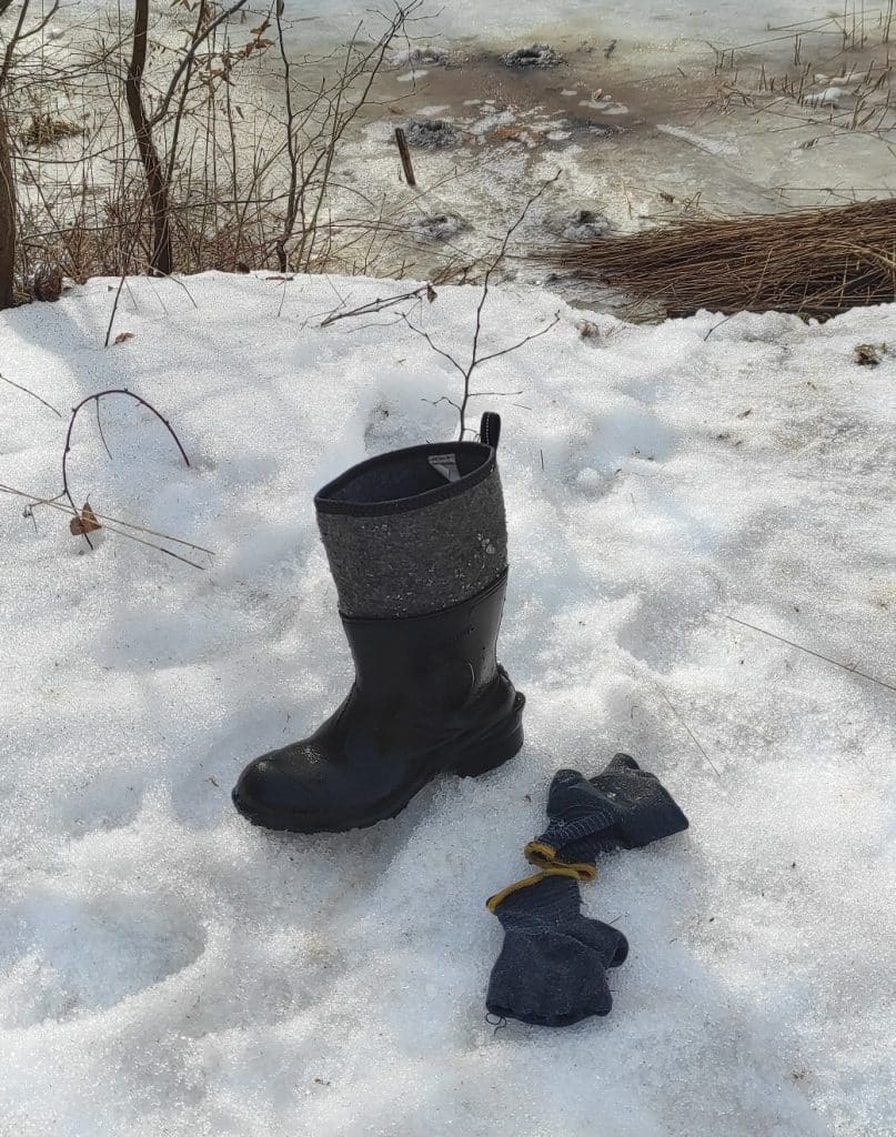 Buty i rękawice na śniegu przy brzegu rzeki, w tle woda i l&oacute;d.