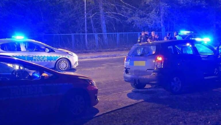 Policja na drodze podczas pościgu za kierowcą, w tle radiowozy z włączonymi światłami.