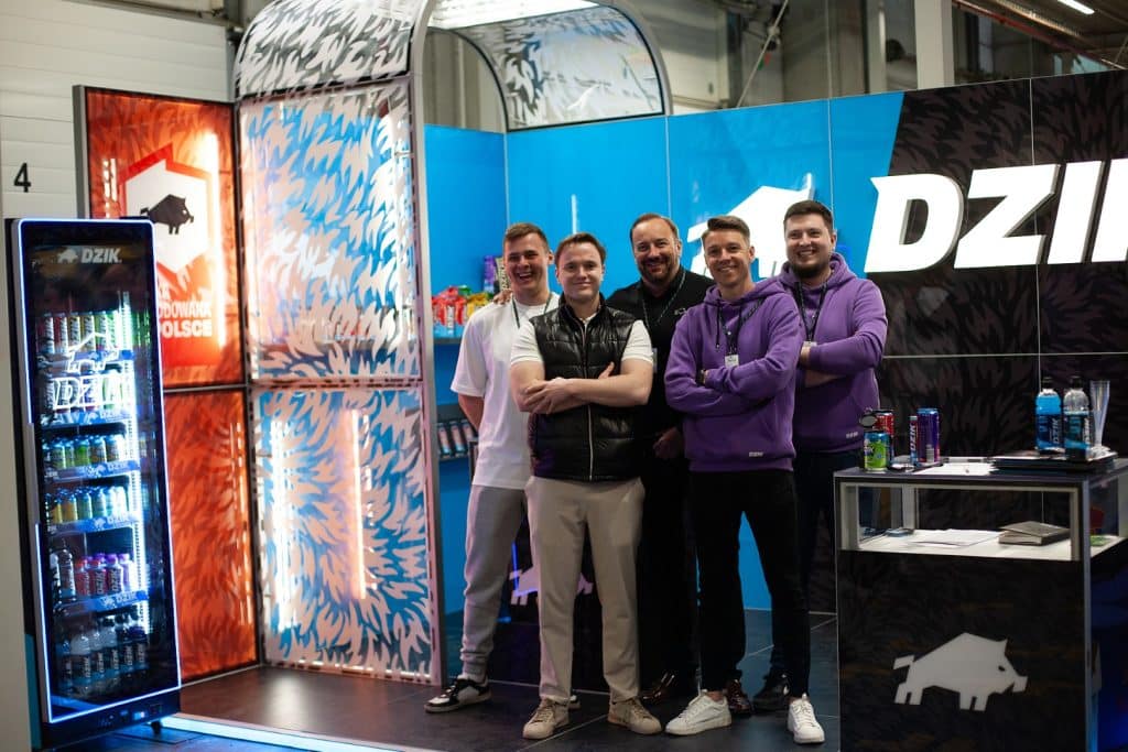 Grupa uśmiechniętych os&oacute;b na stoisku targowym w Gdańsku, z logo Dzik w tle.