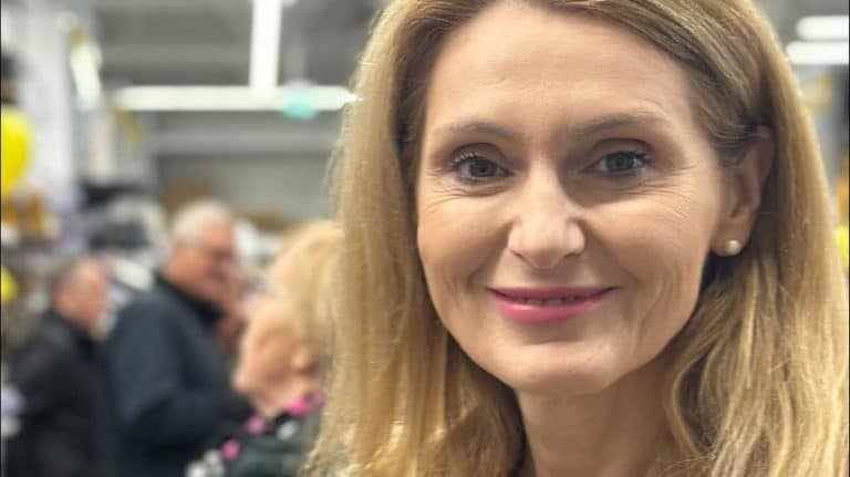 Zdjęcie kobiety z blond włosami i uśmiechem, w tle ludzie w sklepie budowlanym.