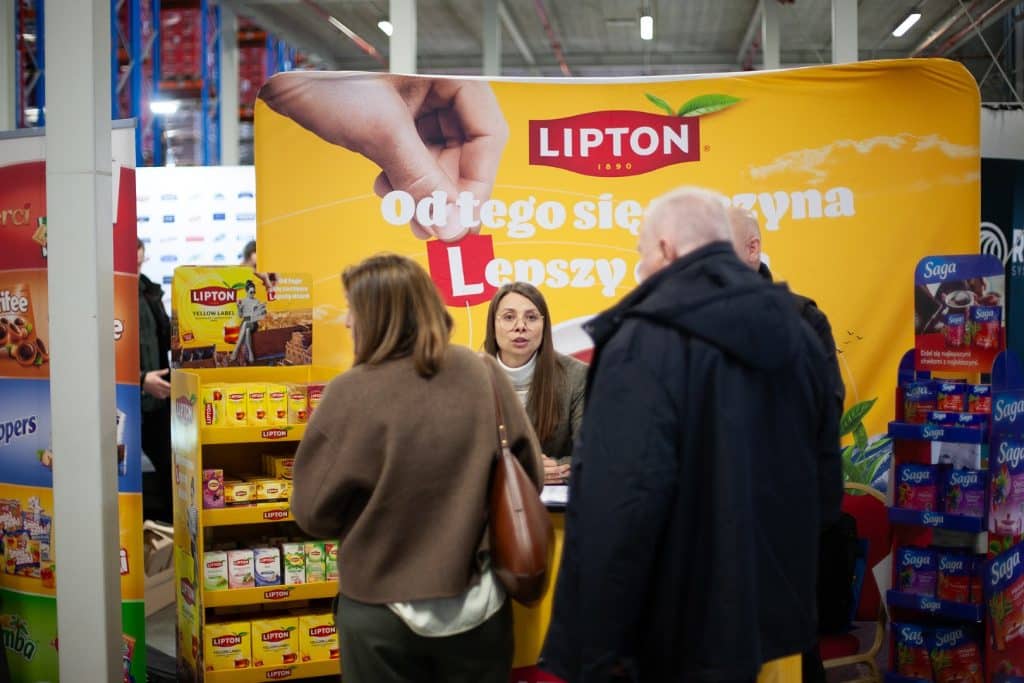 Stoisko z produktami Lipton na targach w Gdańsku, z rozmowami uczestnik&oacute;w przy stanowisku.