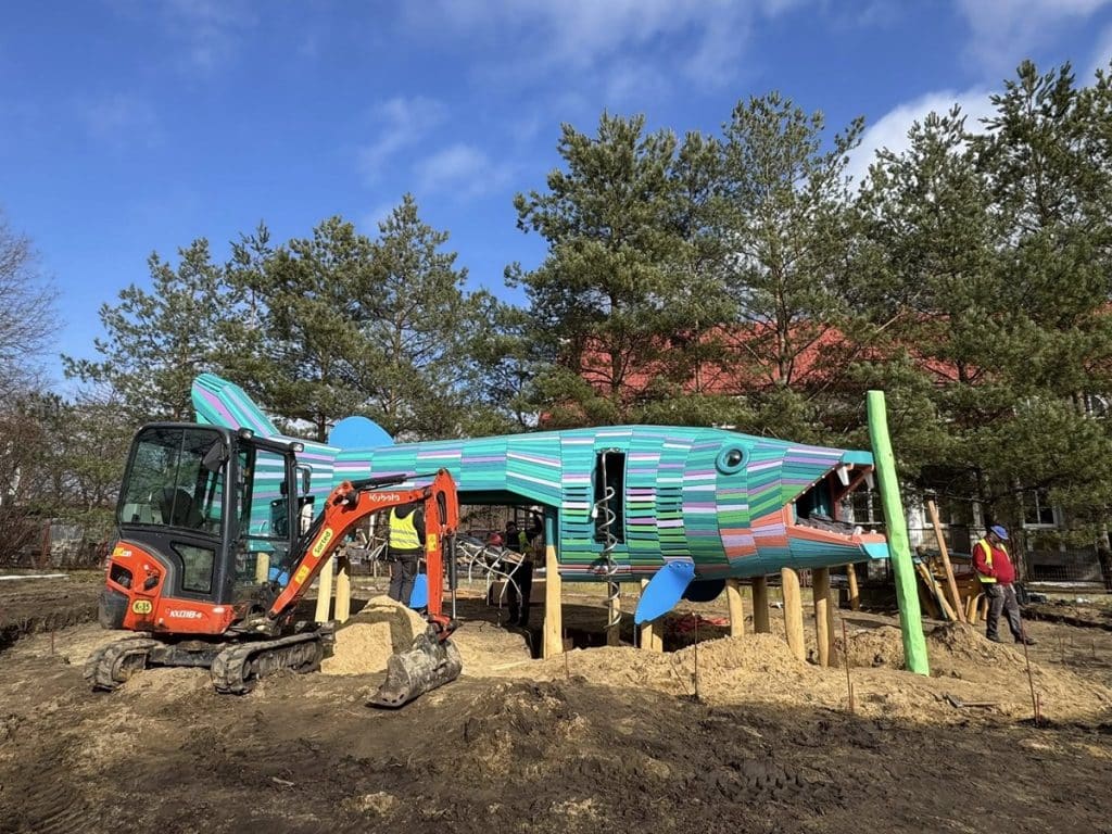 Budowa dużej, kolorowej rzeźby szczupaka na placu w Giżycku, wok&oacute;ł prace budowlane i maszyny.