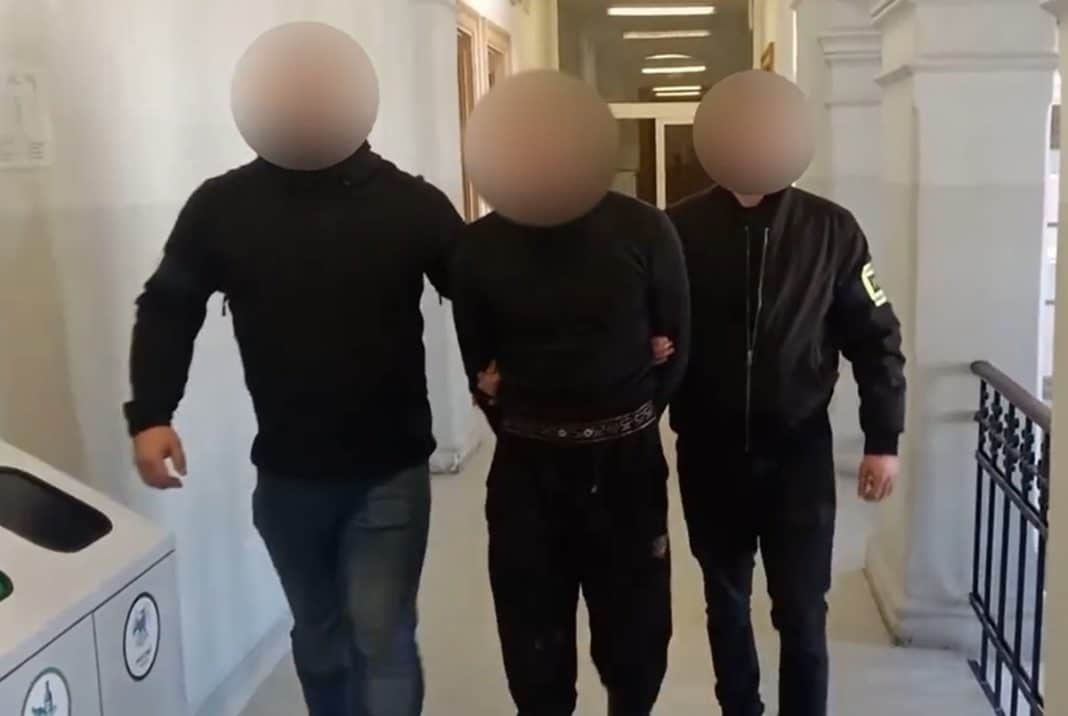 Mężczyzna w rękach policjant&oacute;w w budynku, twarze zamazane, w tle klatka schodowa.