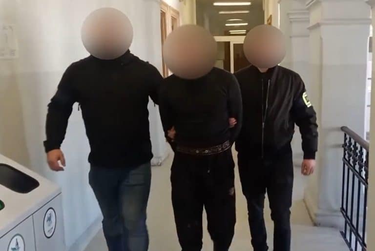 Mężczyzna w rękach policjant&oacute;w w budynku, twarze zamazane, w tle klatka schodowa.