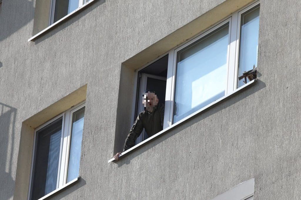 Mężczyzna wychylający się z okna na wysokim piętrze budynku, wok&oacute;ł służby ratunkowe.