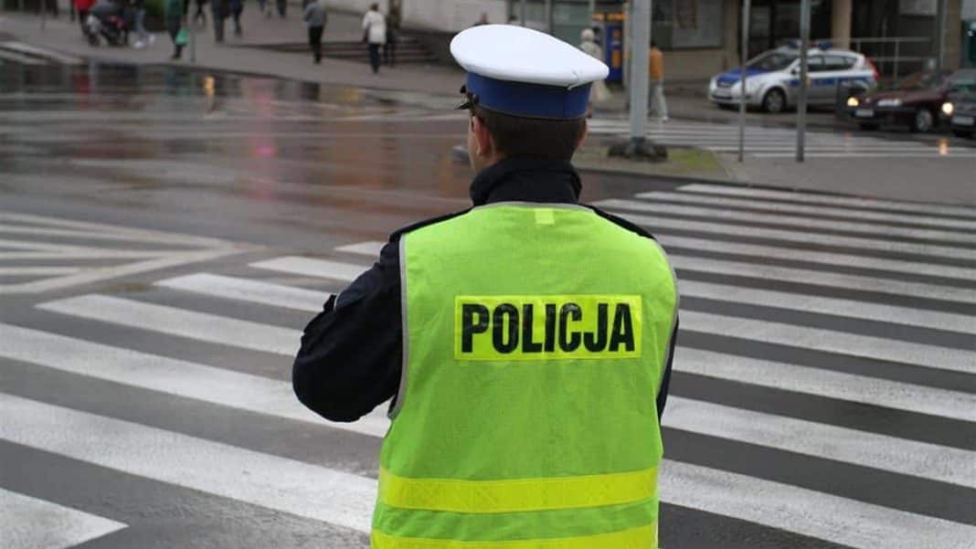 Policjant na przejściu dla pieszych w deszczowy dzień, w tle ruch uliczny i przechodnie.