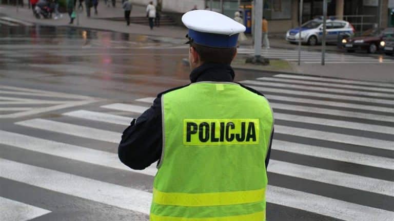 Policjant na przejściu dla pieszych w deszczowy dzień, w tle ruch uliczny i przechodnie.