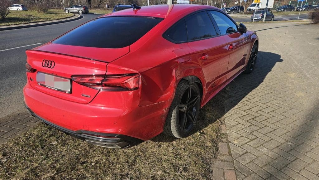 Czerwony samoch&oacute;d marki Audi po dachowaniu na rondzie w Olsztynie, widoczny z tyłu i z boku, na poboczu.