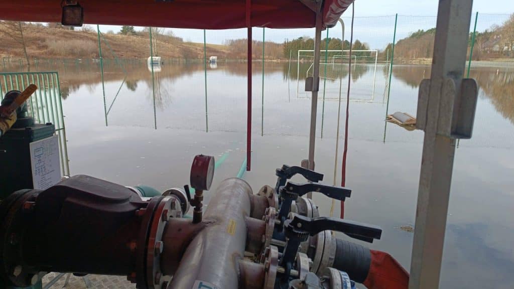 Zalane boisko sportowe we Fromborku, widok z perspektywy na wodę i infrastrukturę.