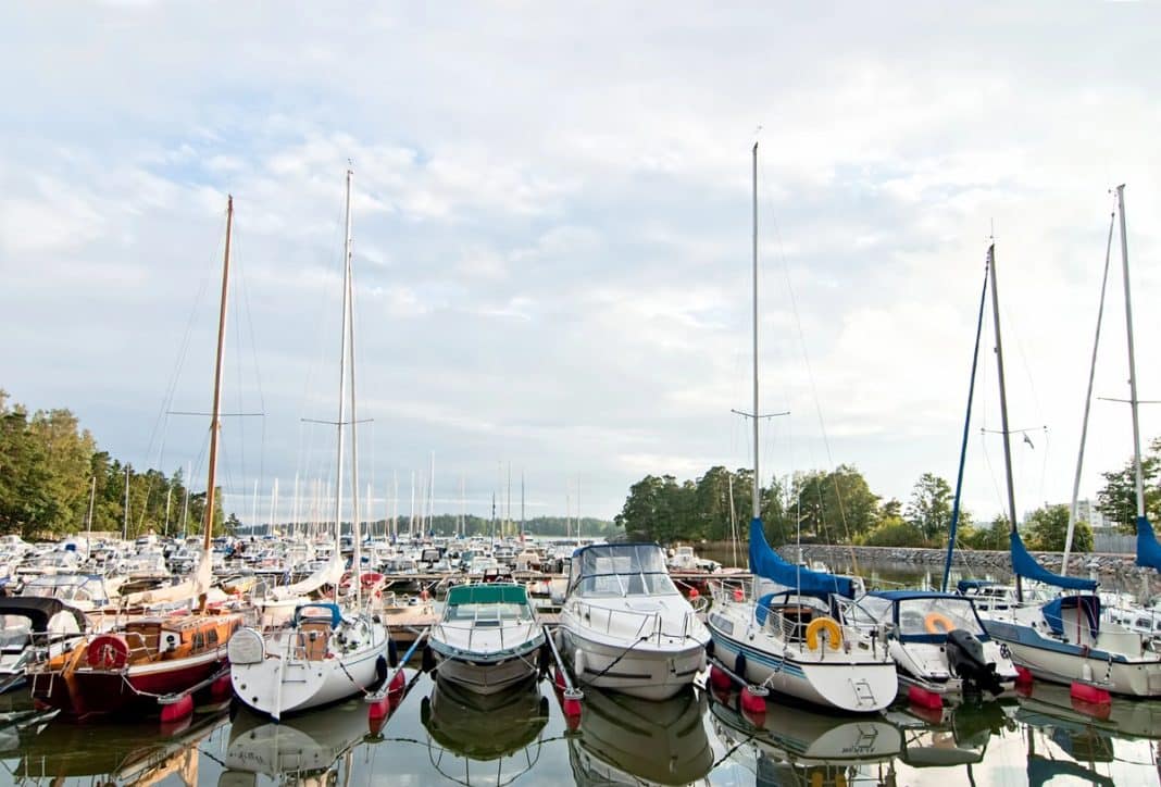 Zdjęcie portu jachtowego na Mazurach z wieloma łodziami na wodzie i w tle lasy.