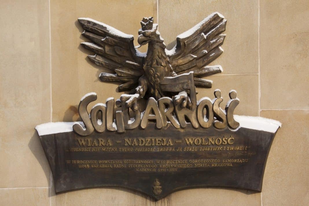 Drewniana tablica z orłem i napisem 'Solidarność' na ścianie, pokryta śniegiem.