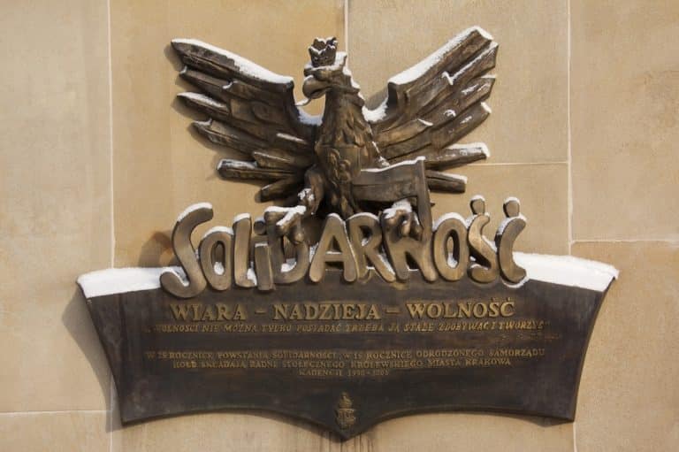 Drewniana tablica z orłem i napisem 'Solidarność' na ścianie, pokryta śniegiem.