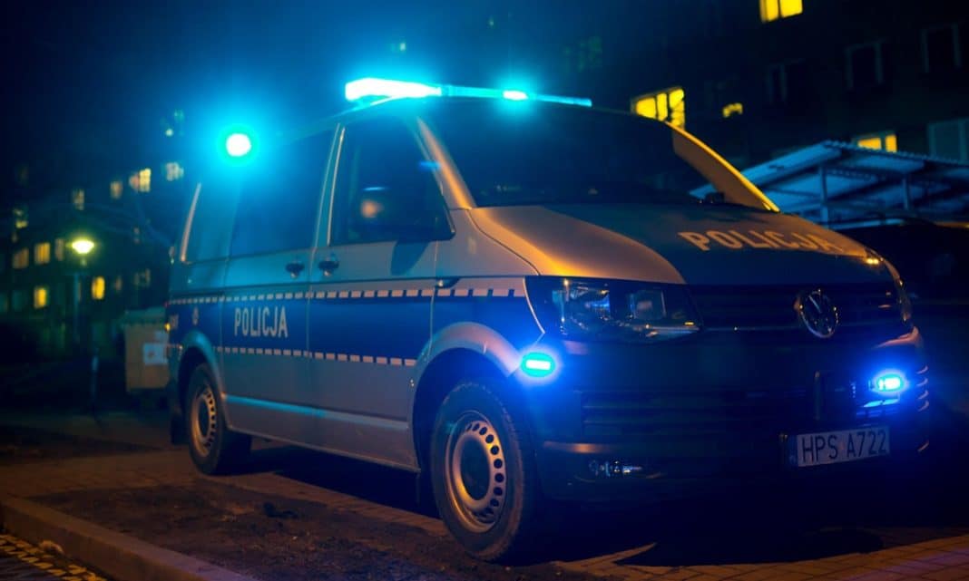 Policja na ulicy w Mrągowie, pojazd z włączonymi światłami w nocy.