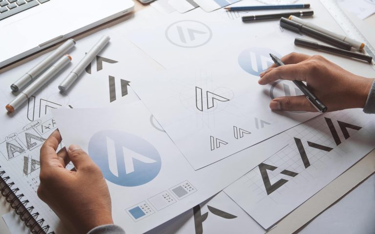 Projektant tworzy logo na papierze, otoczony narzędziami i szkicami.