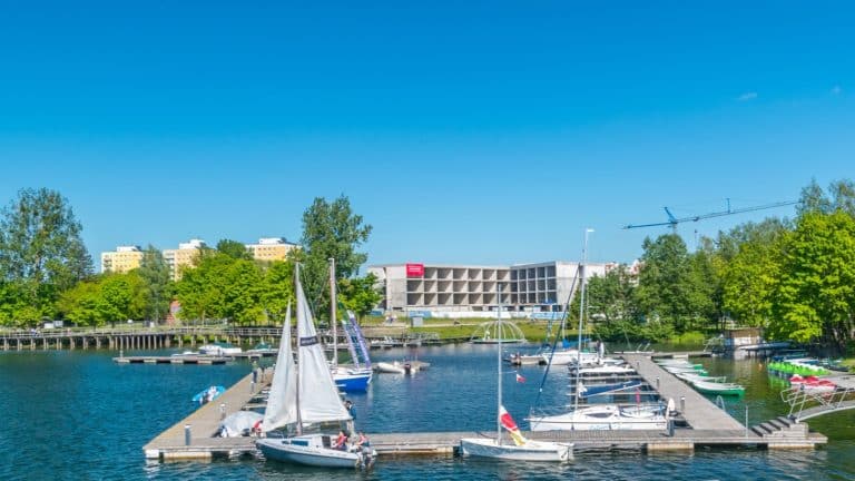 Widok na jezioro Ukiel z łodziami i mariną, w tle zieleń i budynek w budowie.