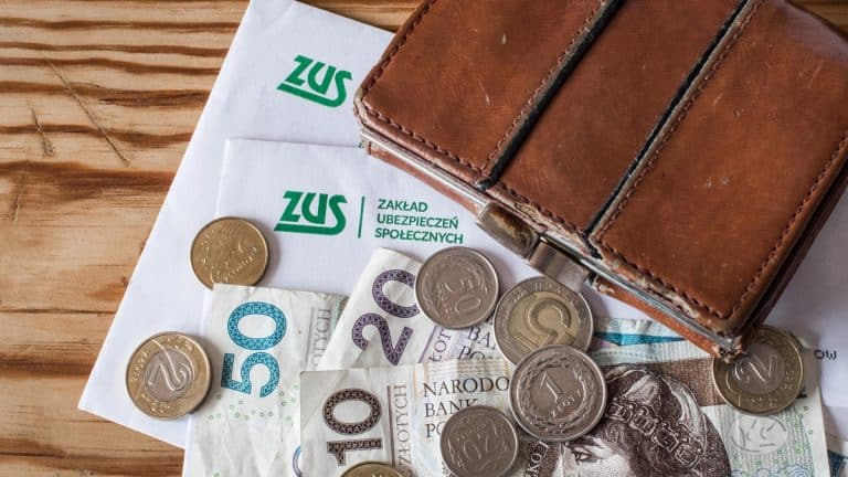 Portfel, banknoty i monety na drewnianym stole, związane z wypłatami ZUS.