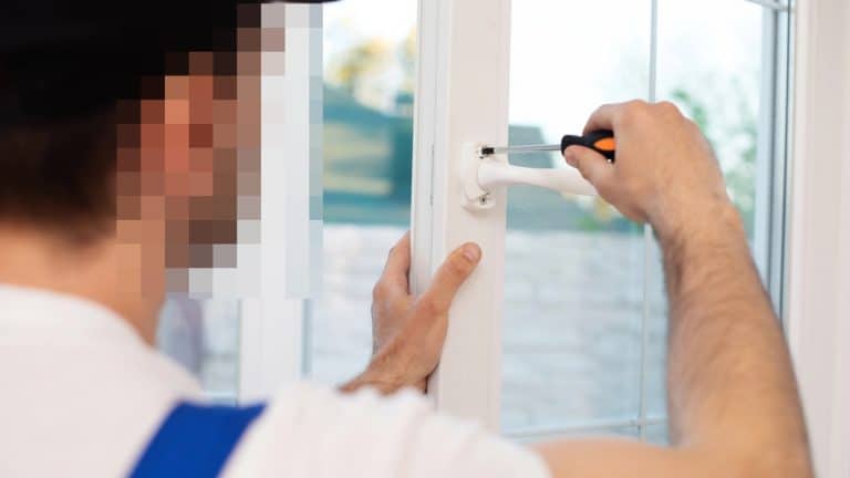 Mężczyzna naprawia okno przy użyciu śrubokręta, z bliska widoczna ręka i narzędzie.