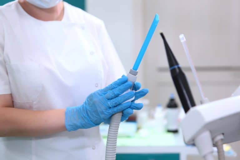 Person w rękawiczkach trzyma urządzenie do dezynfekcji w gabinecie stomatologicznym.