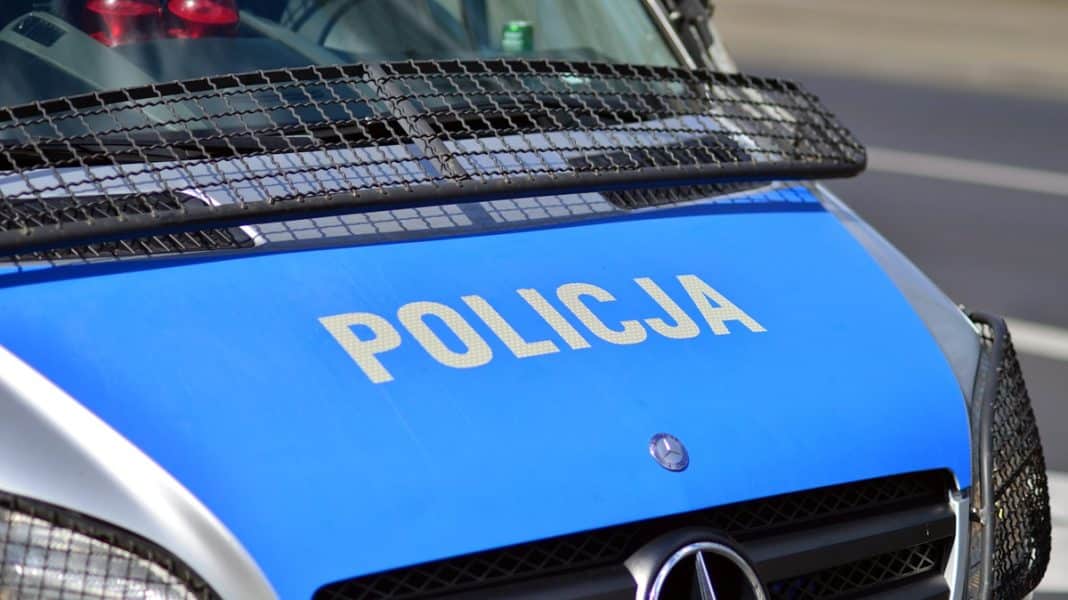 Policja na miejscu zdarzenia, widok na niebieski samoch&oacute;d policyjny z napisem 'Policja'.