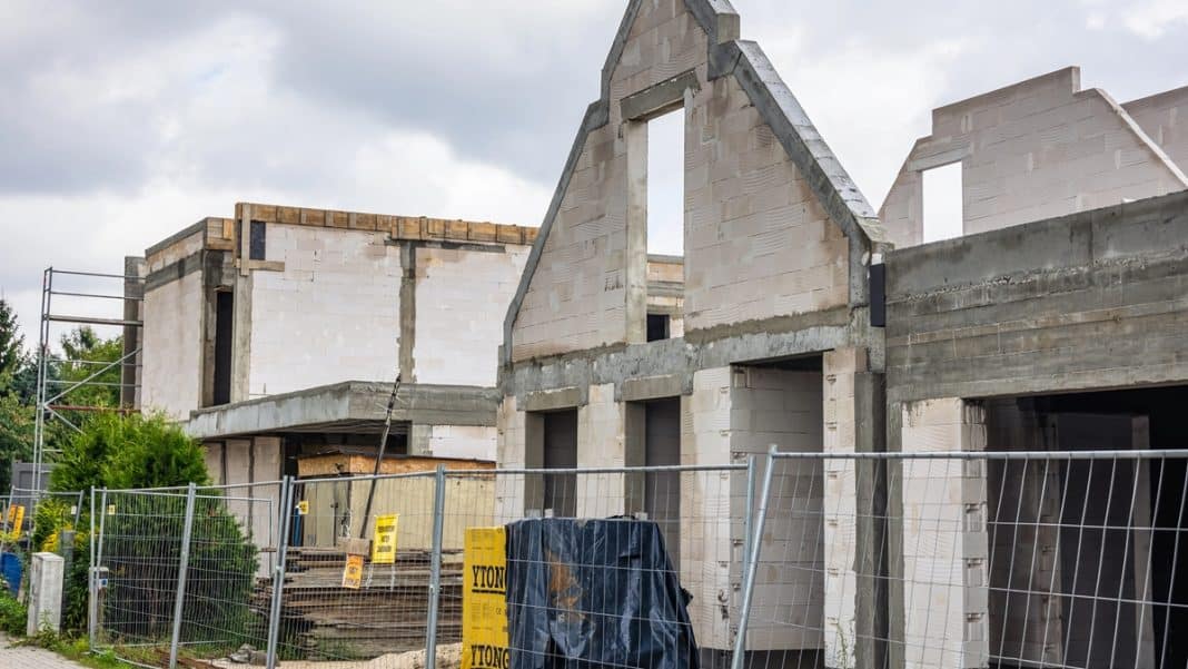 Budowa domu z widokiem na rusztowania i ściany w trakcie wznoszenia, na tle pochmurnego nieba.