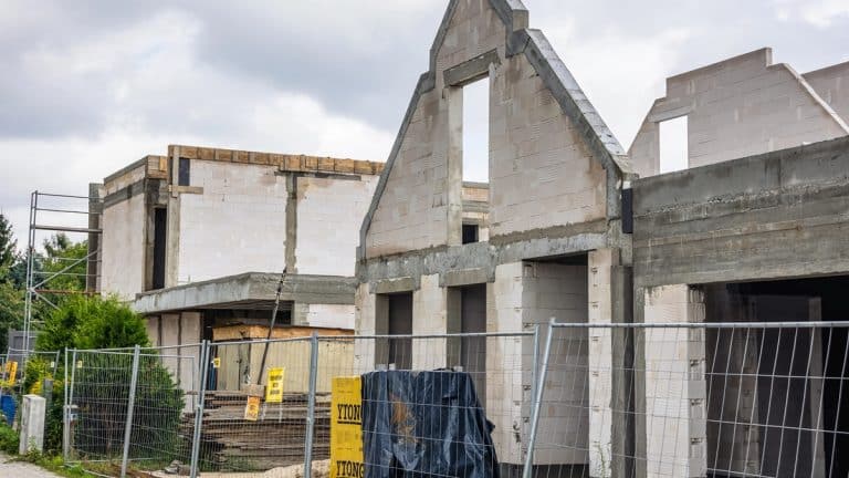 Budowa domu z widokiem na rusztowania i ściany w trakcie wznoszenia, na tle pochmurnego nieba.