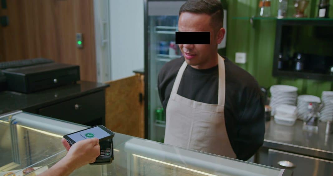 Mężczyzna w kuchni restauracji, obsługa płatności kartą przy ladzie.