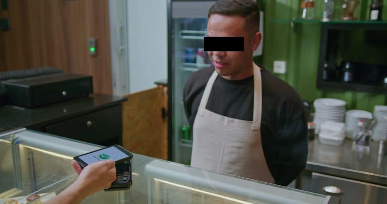 Mężczyzna w kuchni restauracji, obsługa płatności kartą przy ladzie.