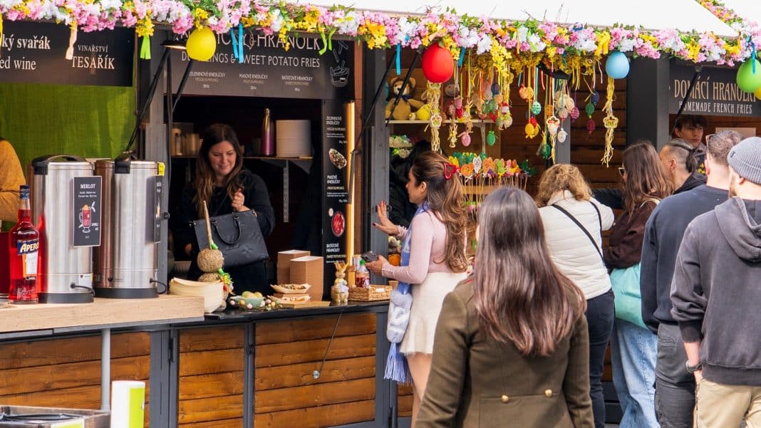 Stoisko z wielkanocnymi dekoracjami i potrawami, ludzie czekają w kolejce na zakupy.