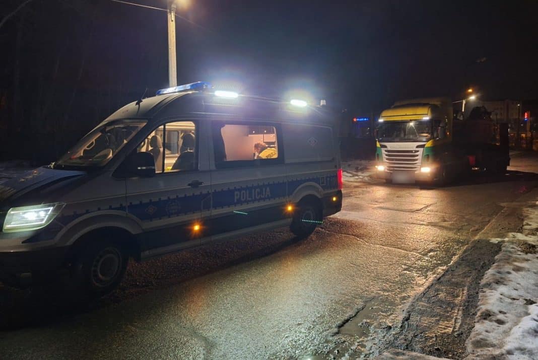 Policja zatrzymuje pojazd na pustej ulicy nocą, w tle inne samochody i oświetlenie miejskie.