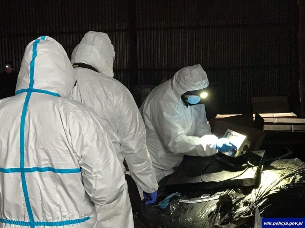 Grupa os&oacute;b w kombinezonach ochronnych pracuje przy zabezpieczaniu laboratorium na Mazurach.