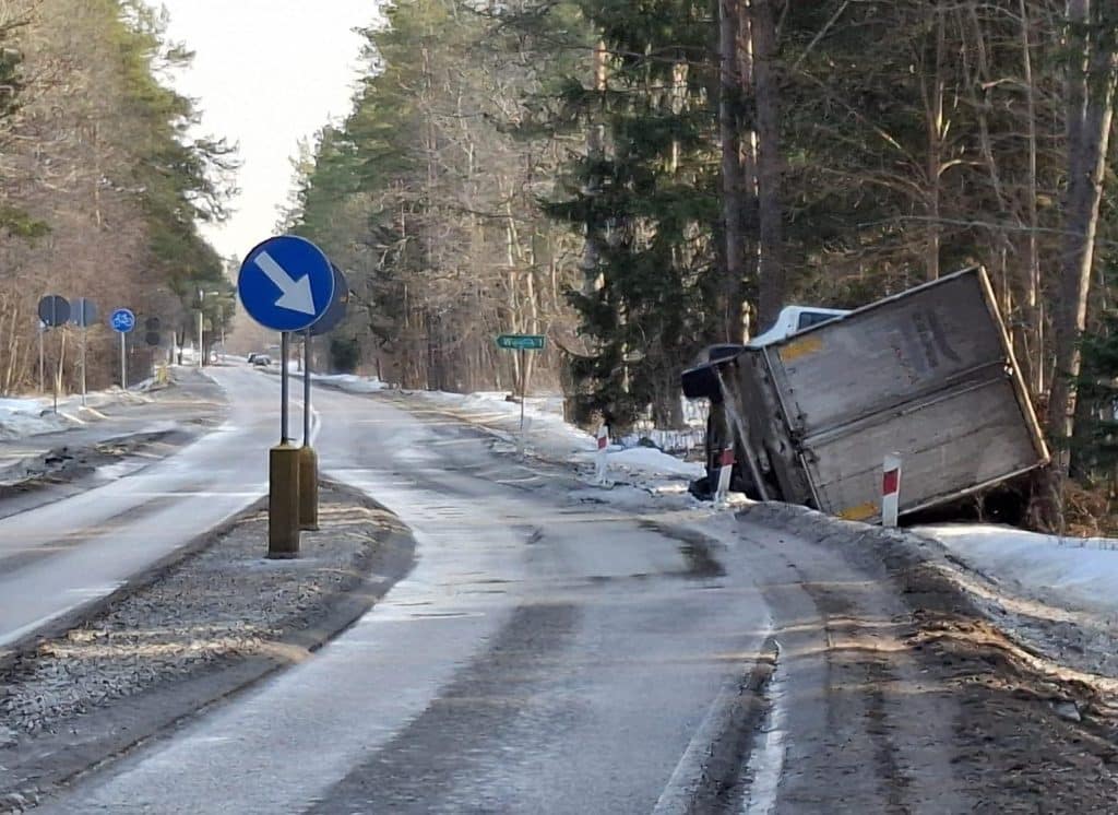 Rozbity samoch&oacute;d ciężarowy w rowie przy zaśnieżonej drodze w lesie.