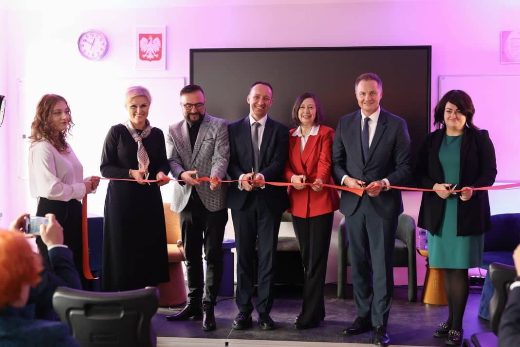 Grupa ludzi podczas oficjalnego otwarcia centrum szkoleniowego w Olsztynie, z czerwonymi nożyczkami.