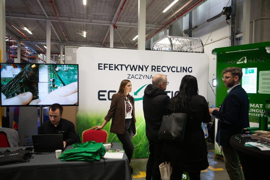 Uczestnicy targ&oacute;w biznesowych w Gdańsku rozmawiają przy stoisku z ekologicznymi rozwiązaniami recyklingowymi.