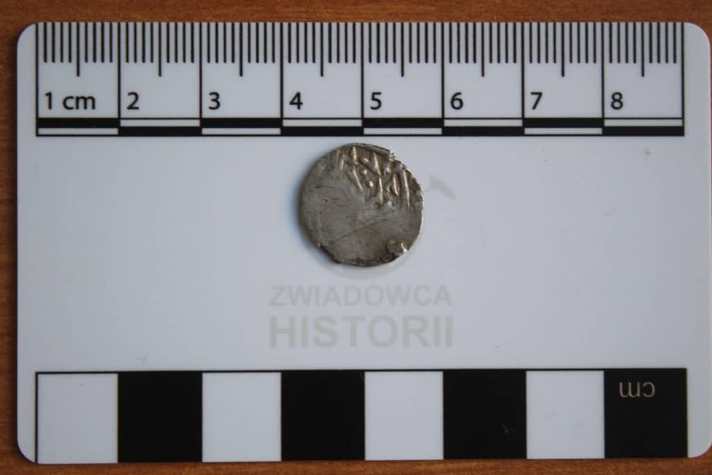 Odkryta moneta tatarska z początku XV wieku na tle miarki, obok tablicy z napisem 'Zwiadowca Historii'.